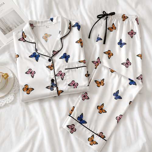 Butterfly print satin pyjama set laid flat on white bed linen, shirt and pants